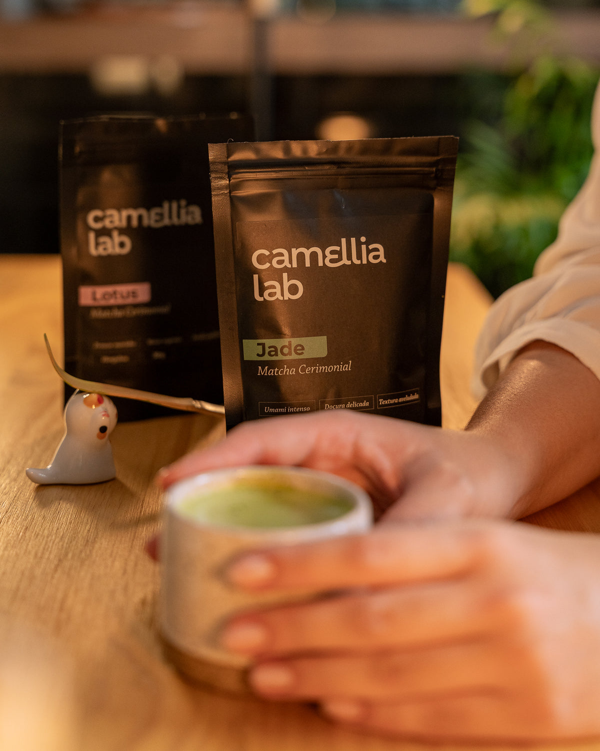 Pacote de matcha cerimonial Jade 30 g ao lado de uma xícara de matcha servida, segurada com as duas mãos