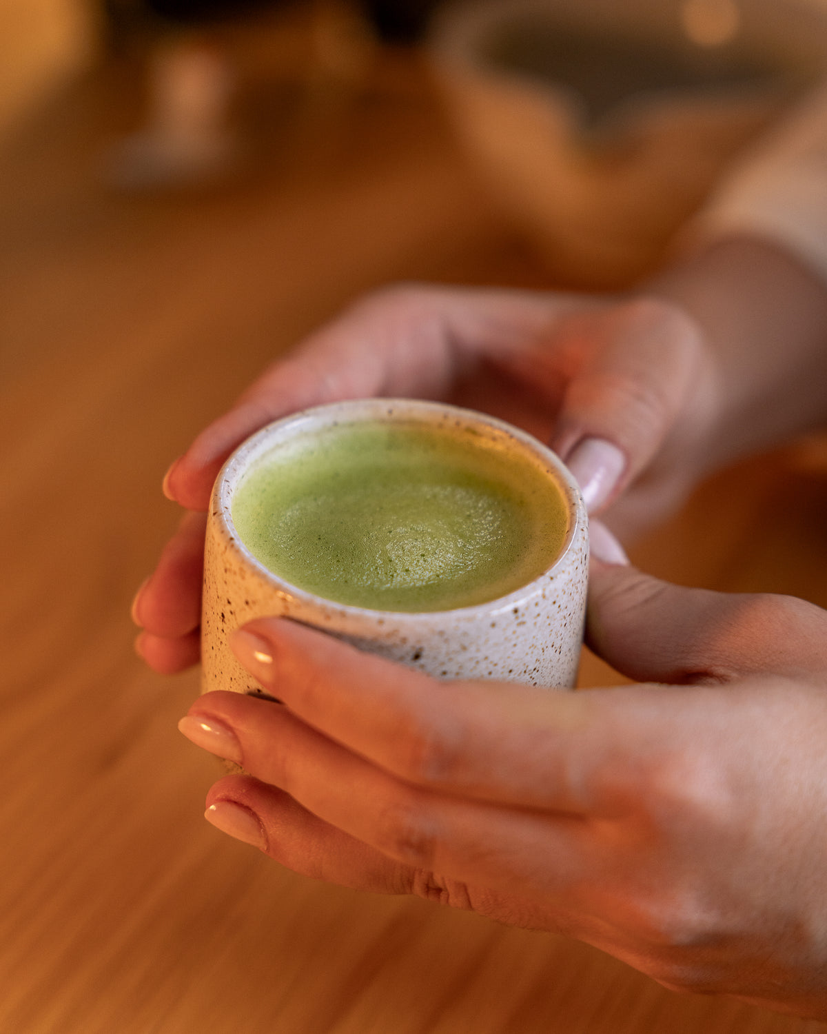 Matcha Lotus preparado quente, com espuma fina, em xícara de cerâmica segurada com as duas mãos